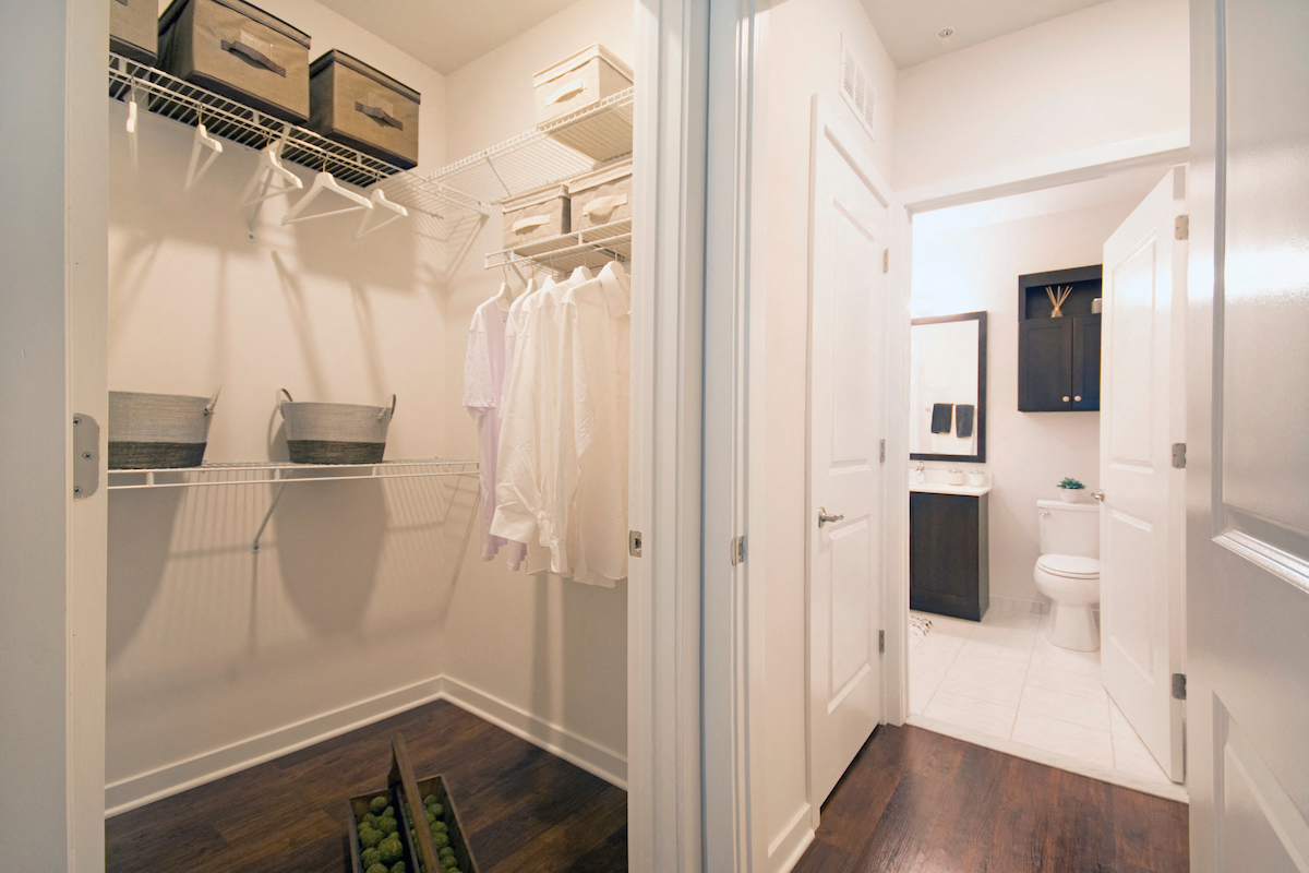 a walk in closet with a mirrored closet door and a white bathroom with a toilet