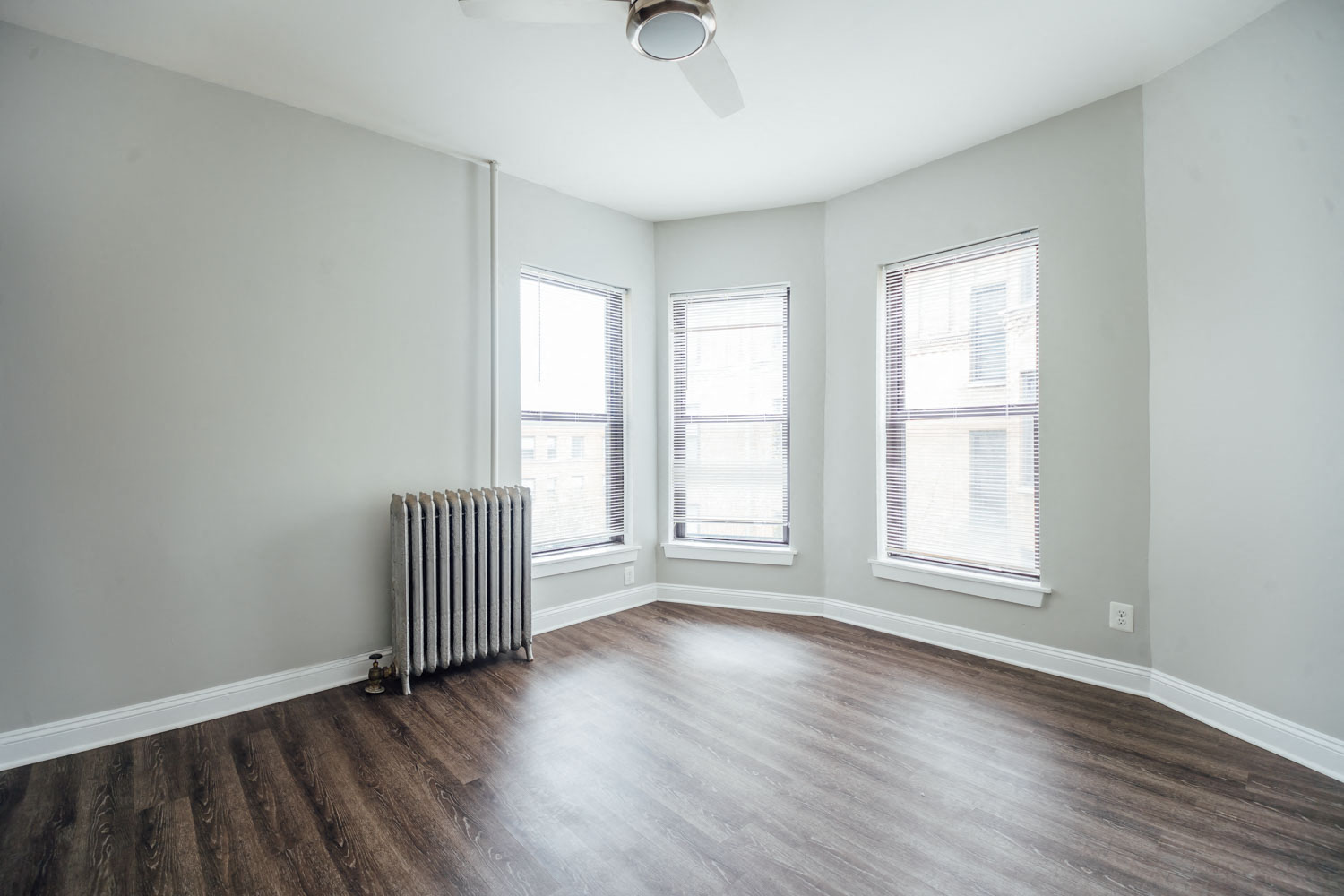 an empty living room with a radiator and three windows