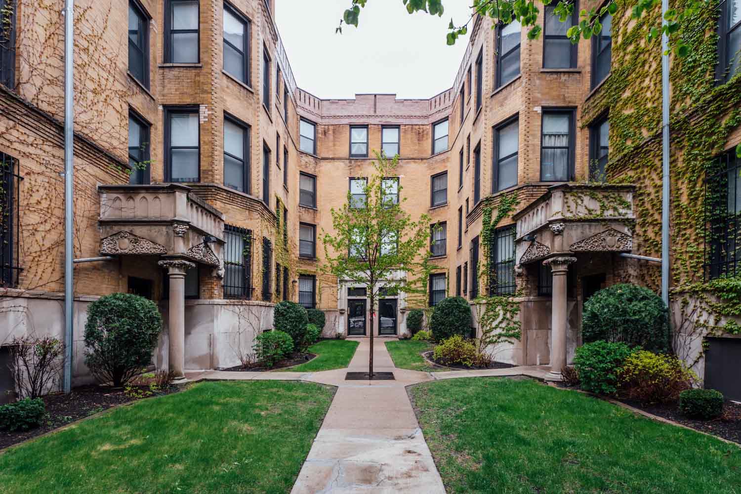exterior view of a brick apartment building with a sidewalk and green lawn