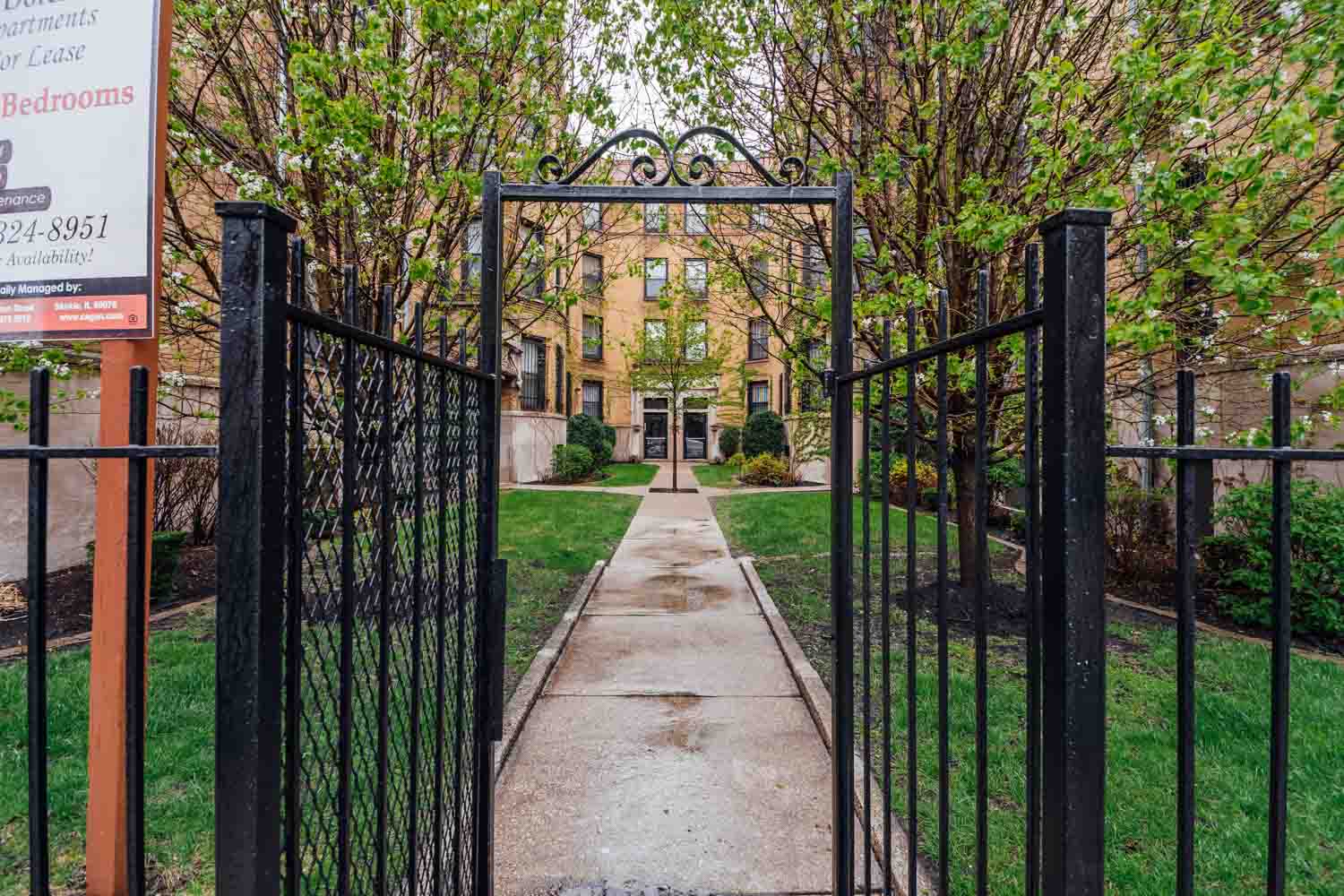 an open gate leading to a sidewalk in front of a building