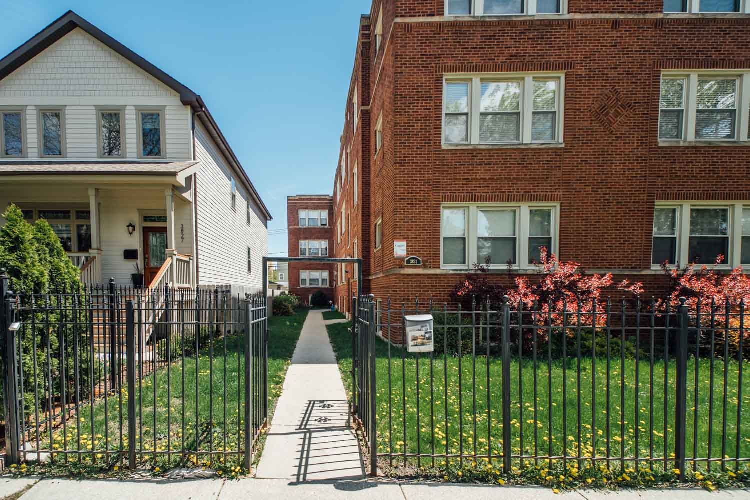 an apartment building with a fence and a sidewalk in front of it