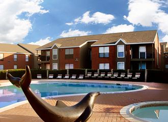 a dolphin statue sits in front of a swimming pool with an apartment building in the background