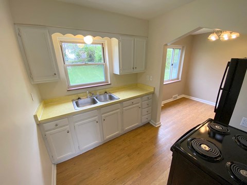 an empty kitchen with white cabinets and a window