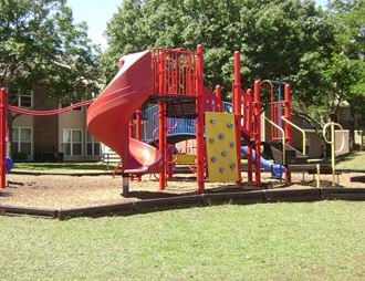 a playground with a red slide and other playground equipment in front of a brick building