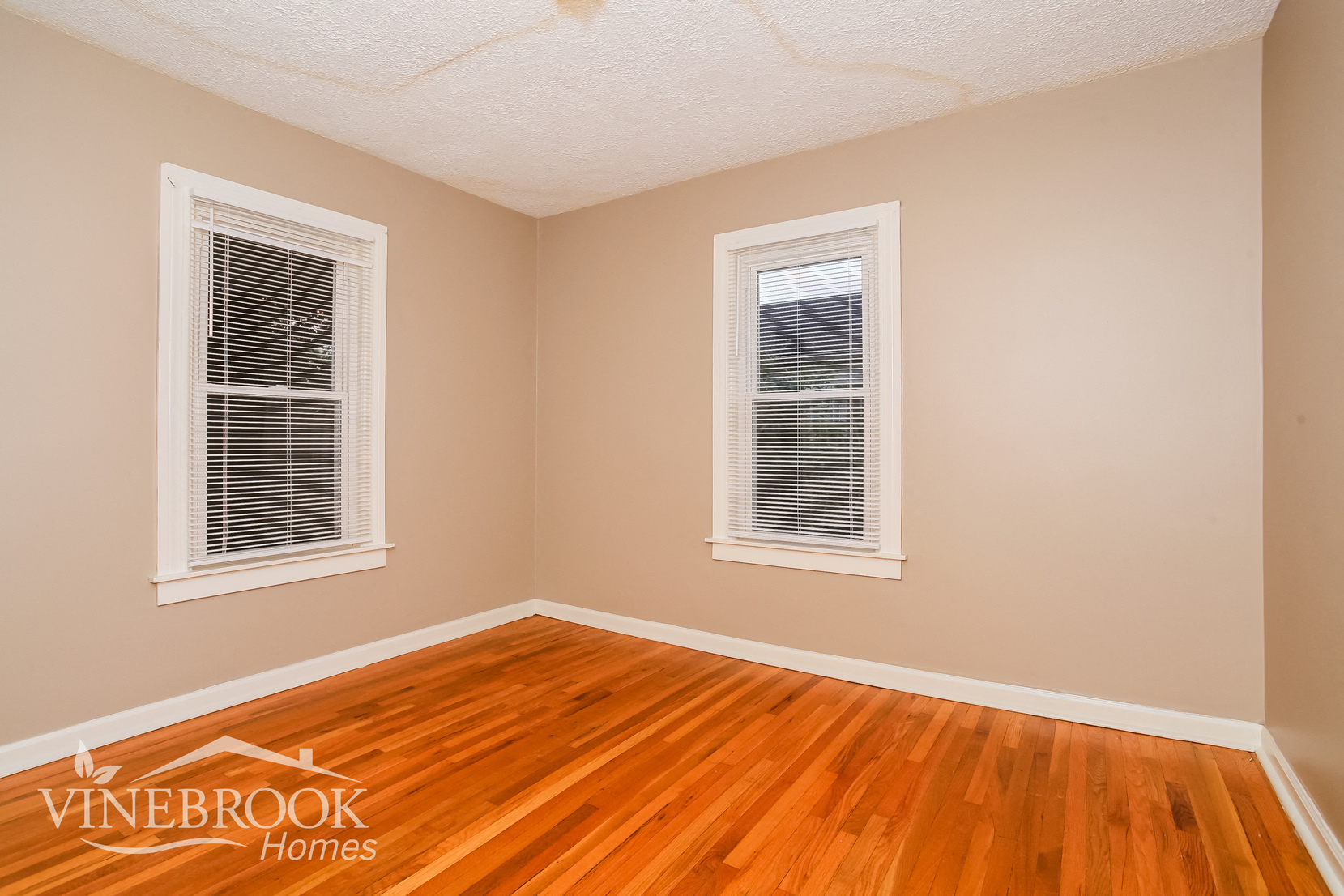 the living room of a home with wood floors and two windows