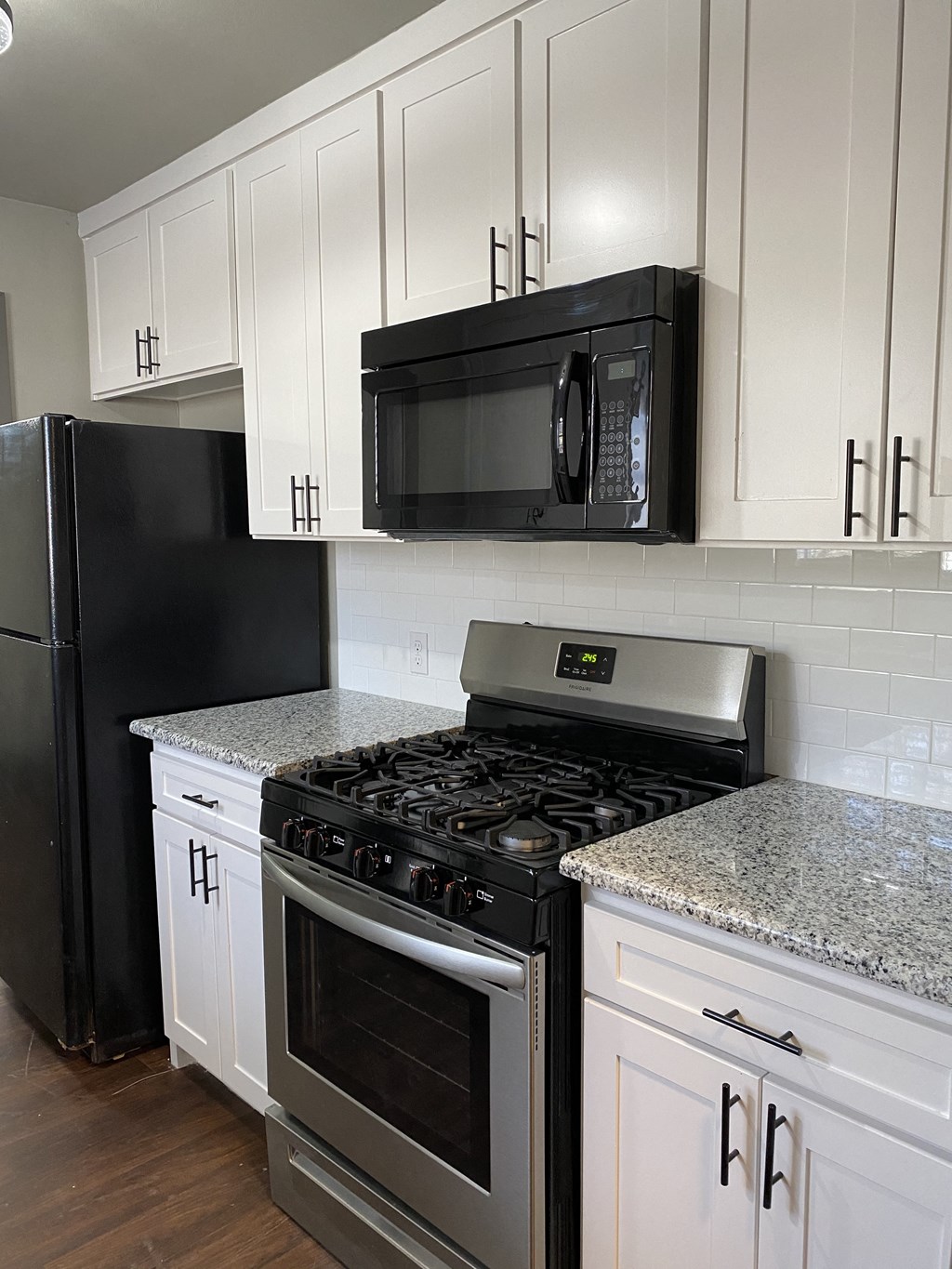 A black microwave is mounted on a white cabinet above a stove.