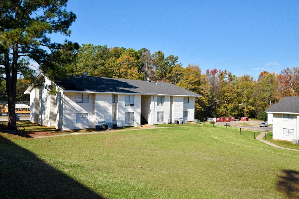 A white building with a black roof is surrounded by a grassy field.