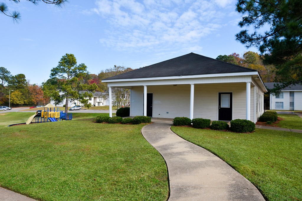 A small white house with a black roof and a playground in the front yard.