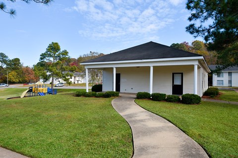 A small white house with a black roof and a playground in the front yard.