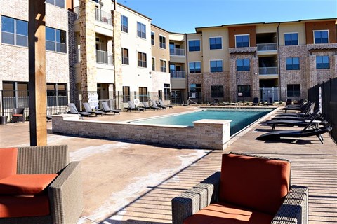A pool surrounded by chairs and a building in the background.