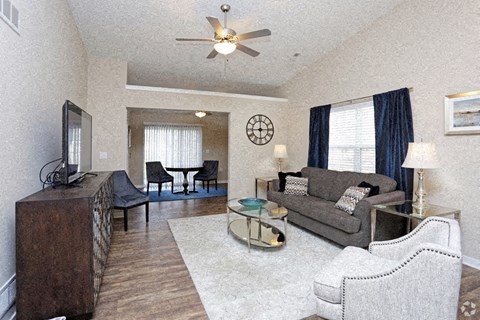 A living room with a grey couch, a black chair, a brown cabinet, and a ceiling fan.