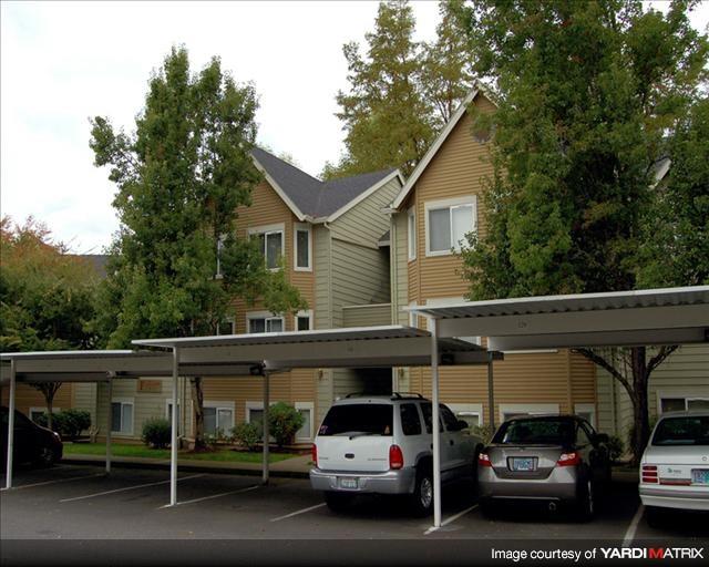A carport with three cars parked in front of a two-story house.