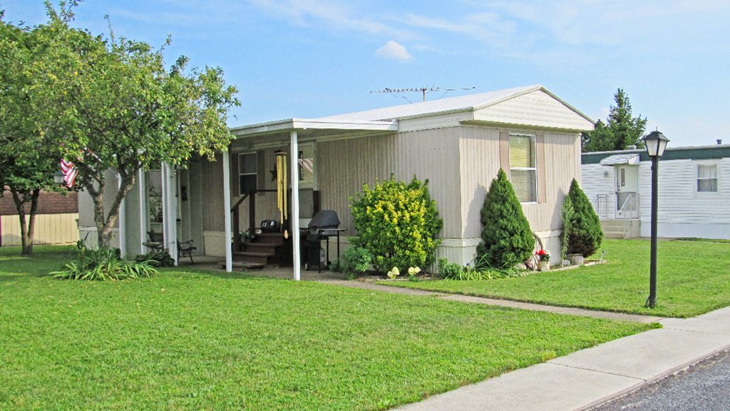 the front of a mobile home with a lawn and a sidewalk
