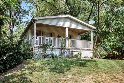 A small white house with a porch is surrounded by trees.