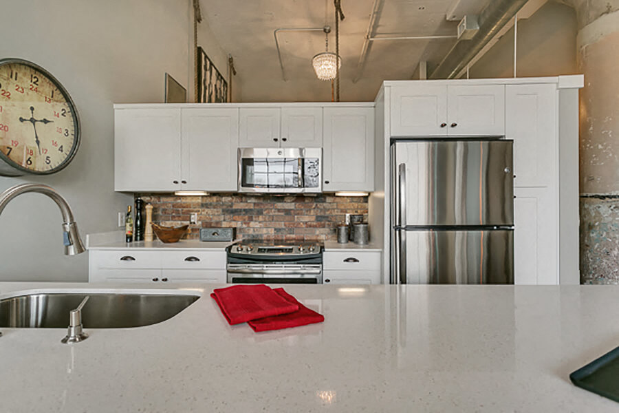 Modern kitchen with white cabinets and brick style backsplash, with white quartz countertop