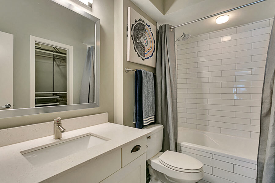 Beautiful modern white bathroom with white subway tiles, soaking tub, and framed mirror with white quartz countertop