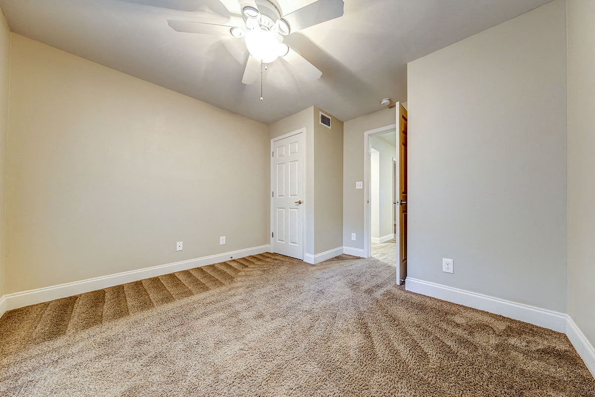 a spacious living room with carpet and a ceiling fan
