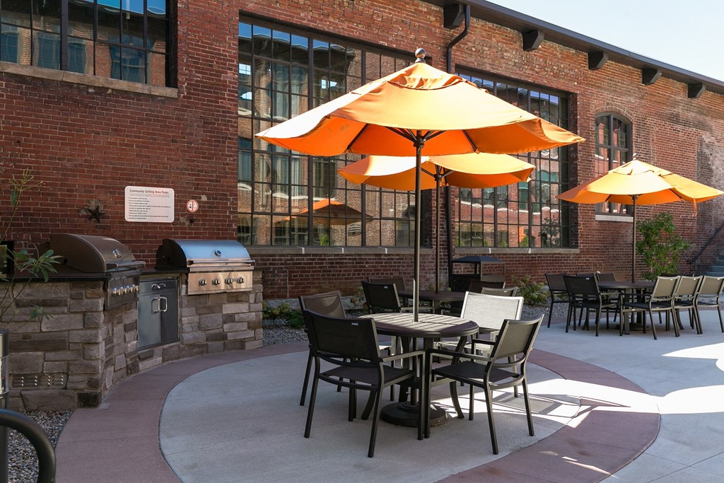 a patio with tables and umbrellas in front of a brick building