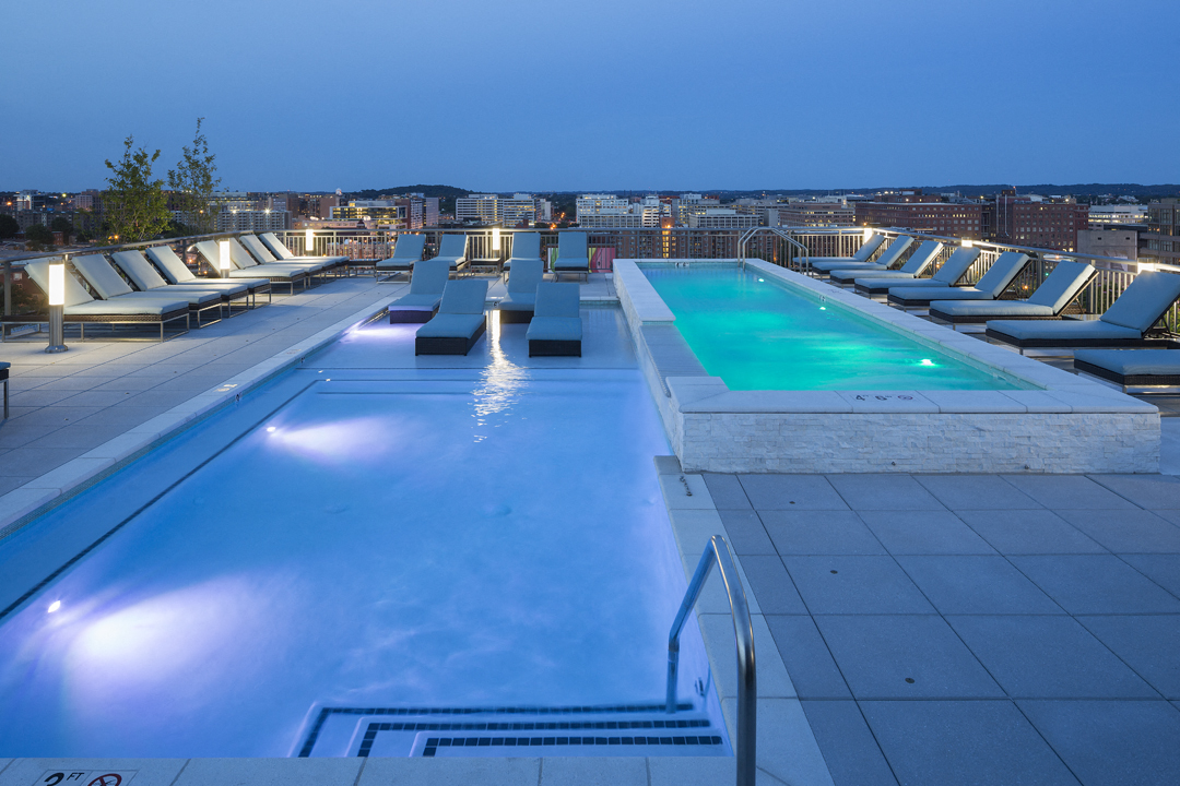 A swimming pool with lounge chairs and a lit poolside area.