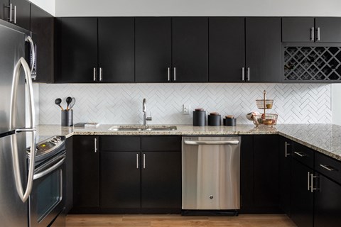 A kitchen with black cabinets and a stainless steel refrigerator.