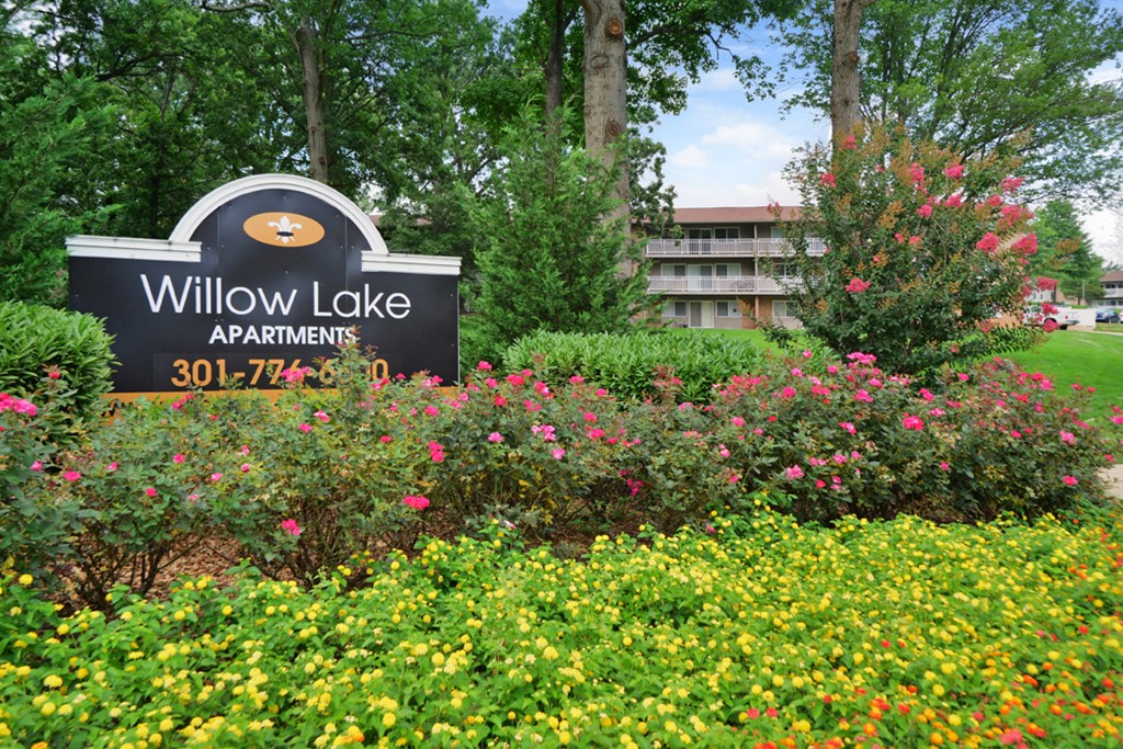 a sign for willow lake apartments in front of a garden of flowers