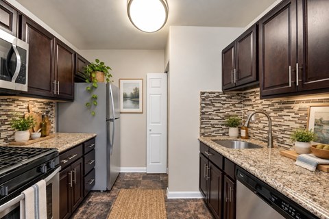 A kitchen with dark brown cabinets and granite countertops.