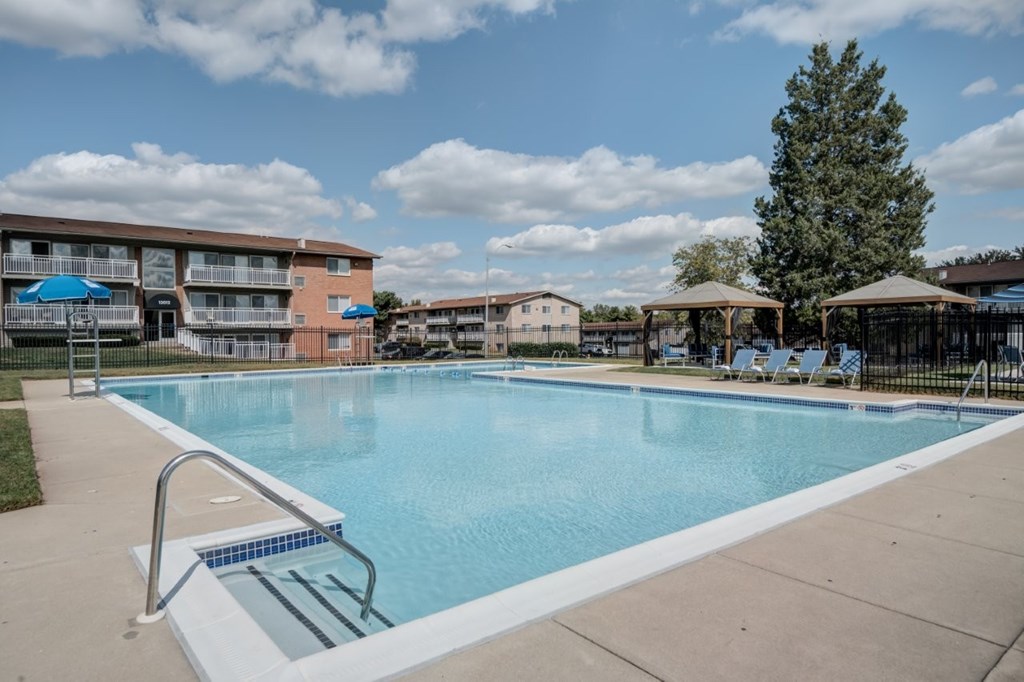 A large swimming pool in front of a building with a blue sky and clouds in the background.