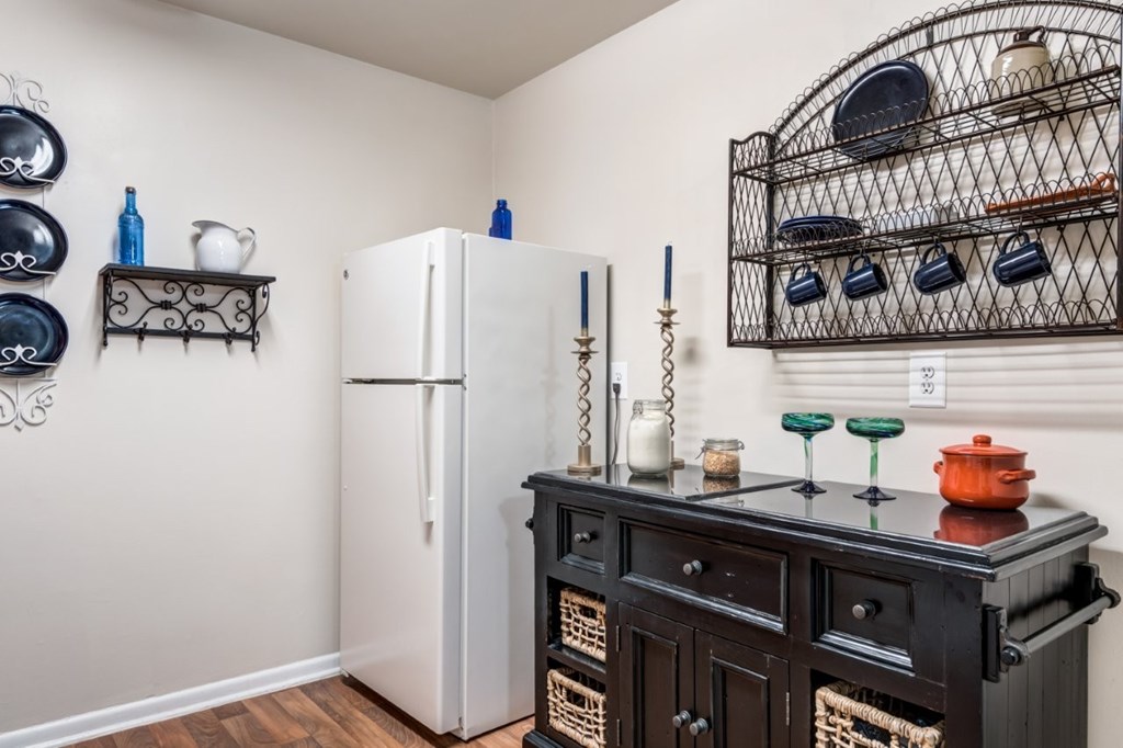 A white refrigerator stands in a kitchen next to a black cabinet with a shelf above it.