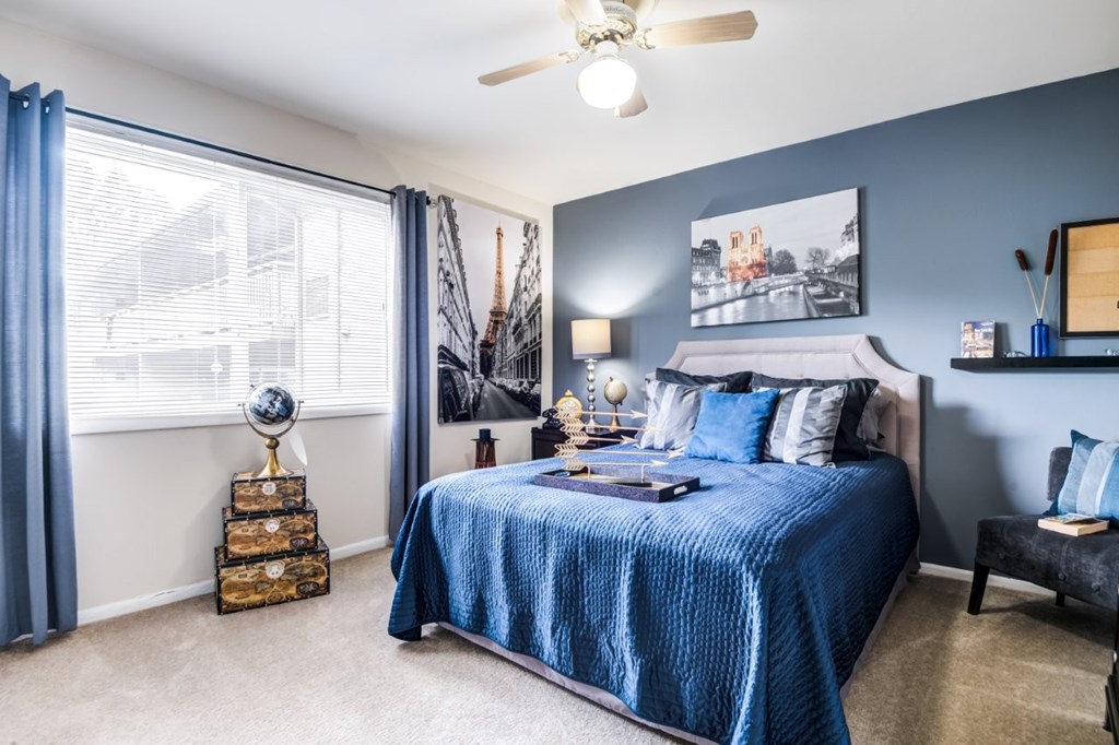 A bedroom with a blue bedspread and a ceiling fan.