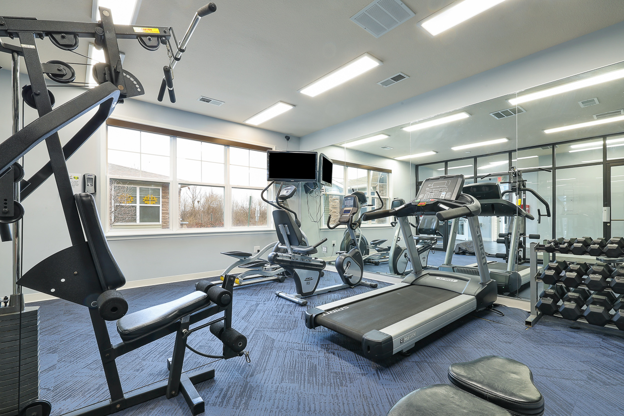 A gym with a variety of equipment including a treadmill, weights, and a bench.