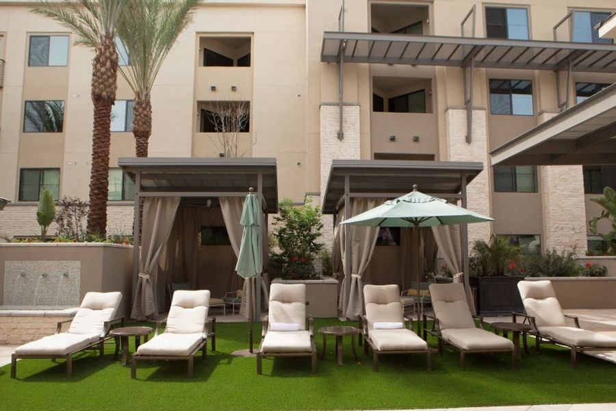 an outdoor lounge area with chairs and umbrellas in front of an apartment building