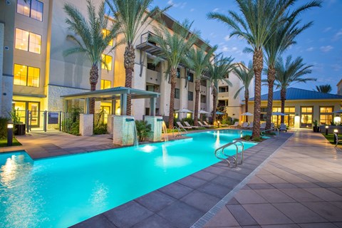 A swimming pool surrounded by palm trees and a building in the background.