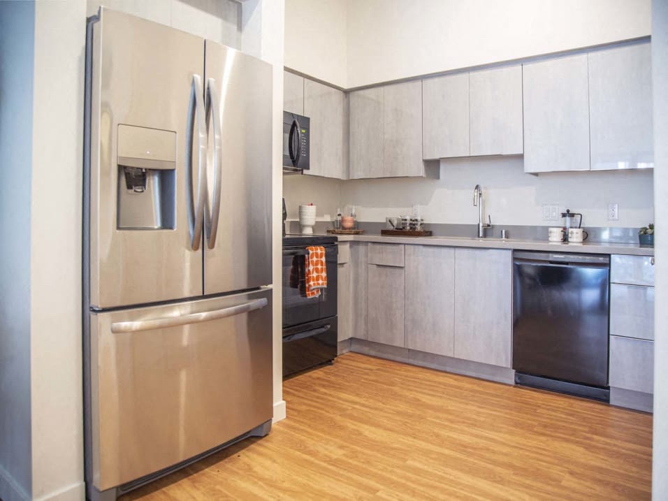 A modern kitchen with a stainless steel refrigerator and wooden flooring.