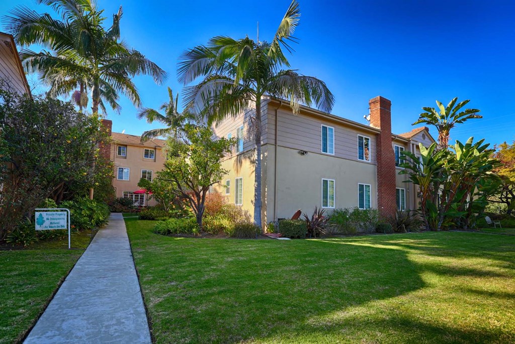 a building with palm trees and a sidewalk in front of it