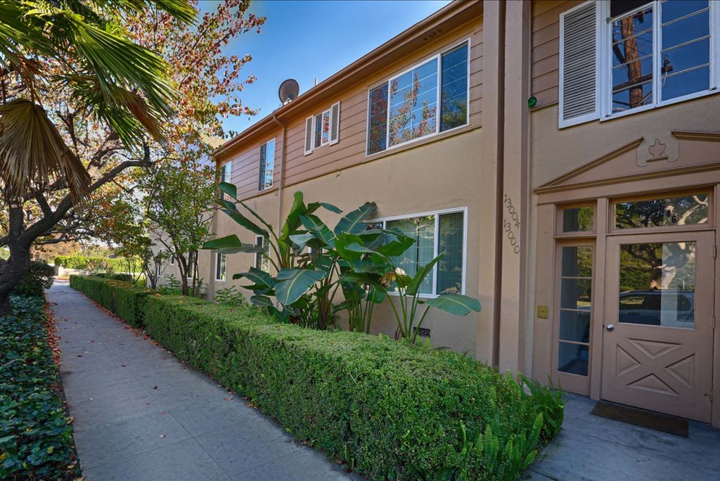 the side of a building with a sidewalk and hedges