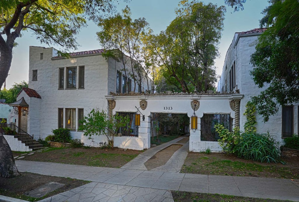 the exterior of a white house with trees and a sidewalk