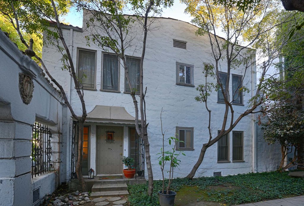 the front of a white house with trees and a sidewalk