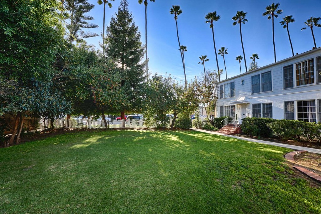 the backyard of a white house with a lawn and palm trees