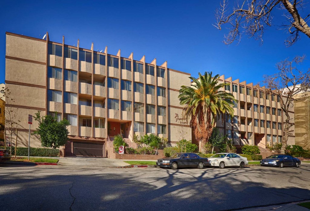 a large building with a palm tree and cars parked in front