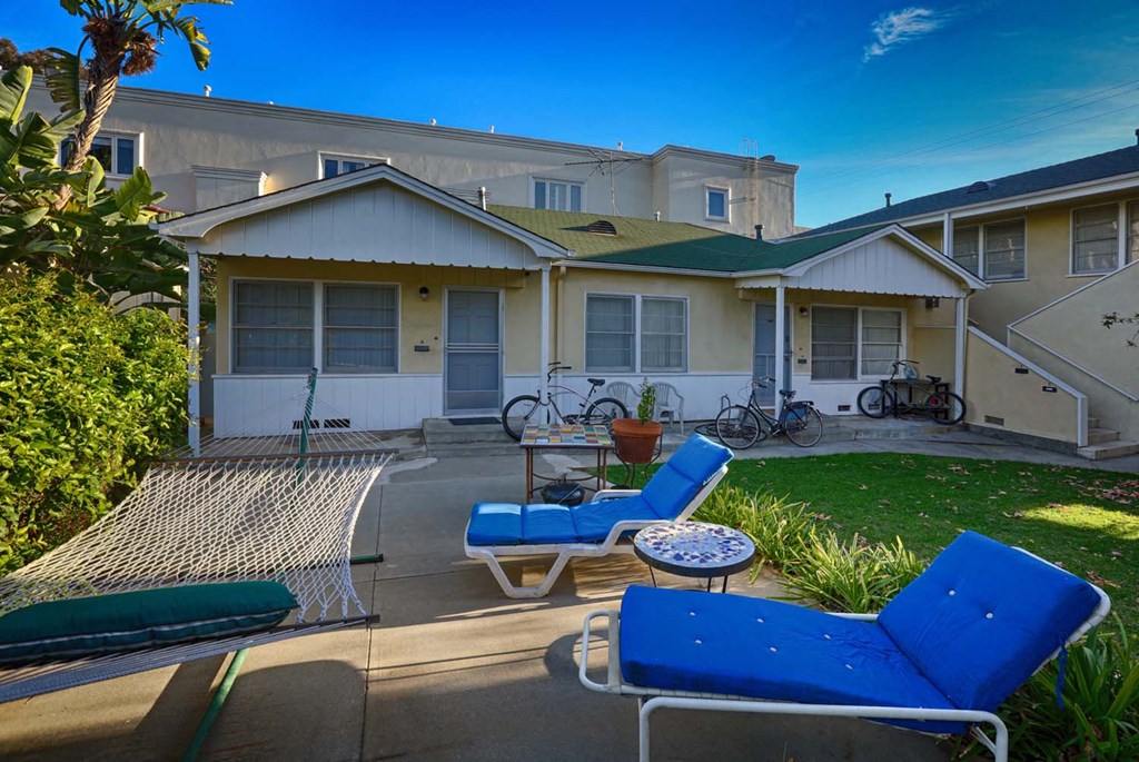 a patio with chairs and a hammock in front of a house