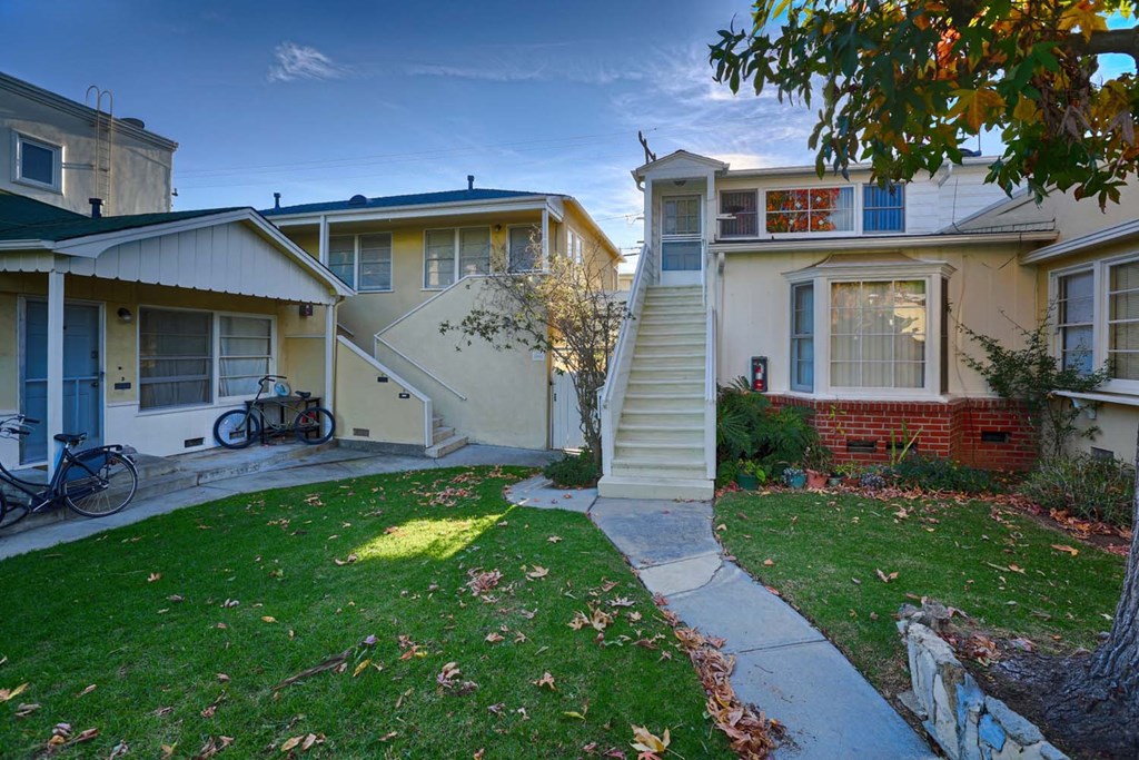 the front yard of an apartment building with stairs and a lawn