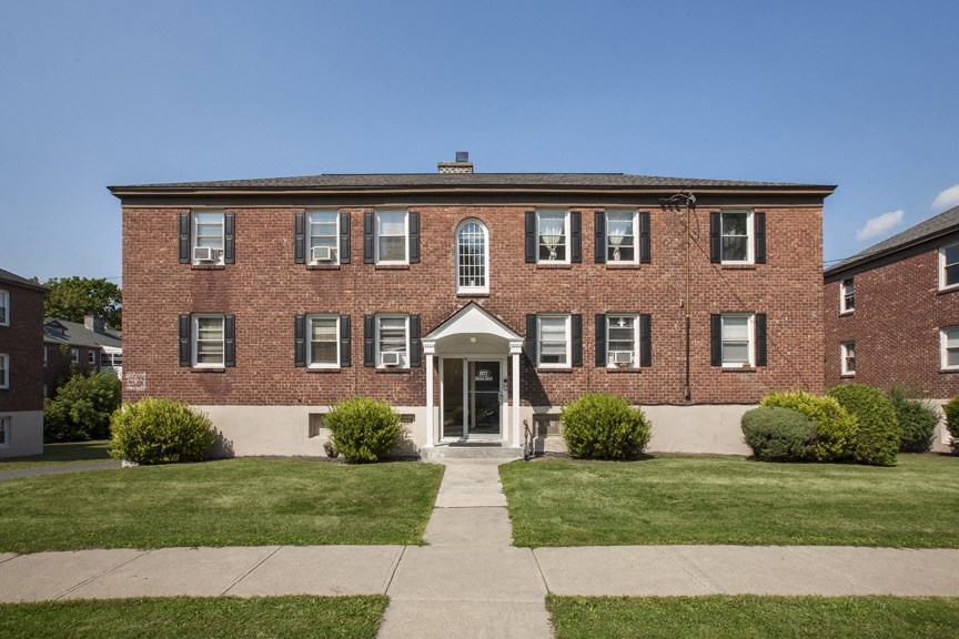 the front of a brick building with a sidewalk and grass