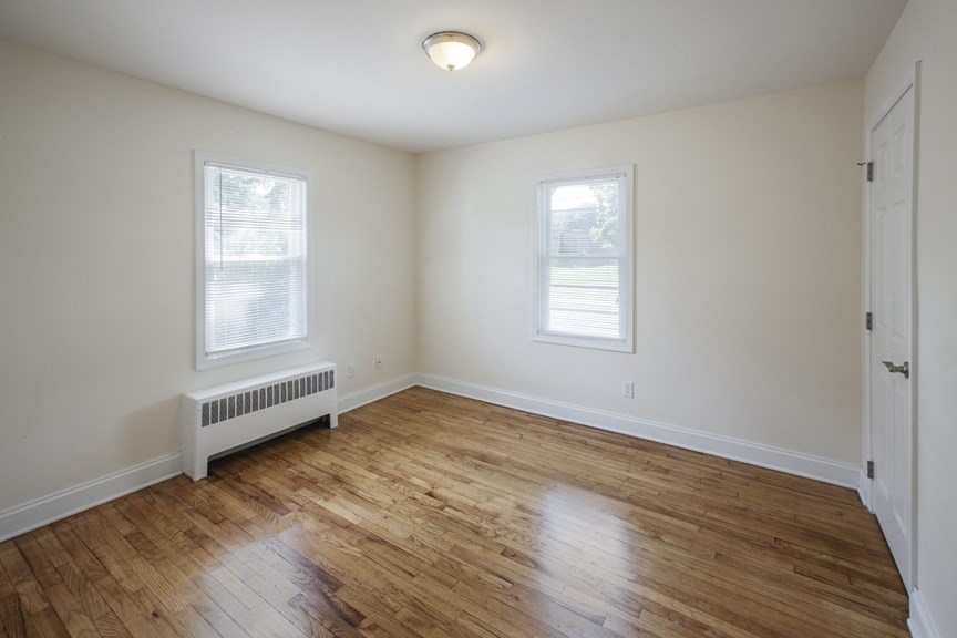 the living room of an empty house with wood flooring and two windows