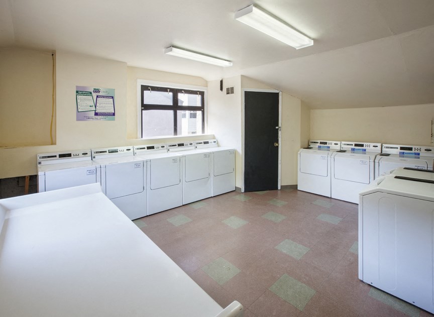 an empty laundry room with white washers and dryers and a window