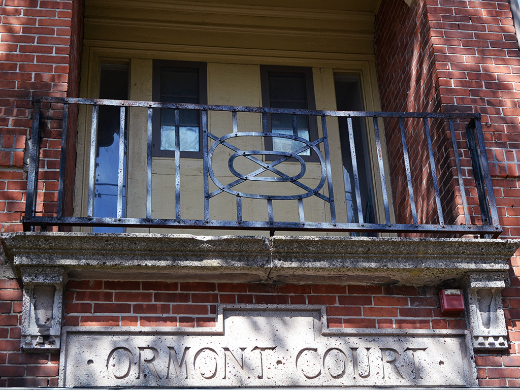 the front door of a brick building with a wrought iron balcony