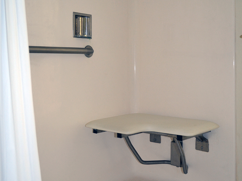 a small desk in a bathroom with a wheelchair rail and a white sink