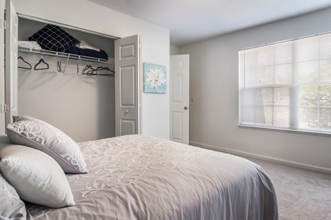 A bedroom with a large bed and a closet with clothes hanging.