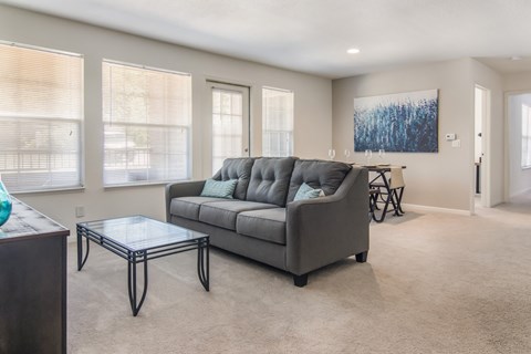 A grey couch with a glass table in front of it in a living room.