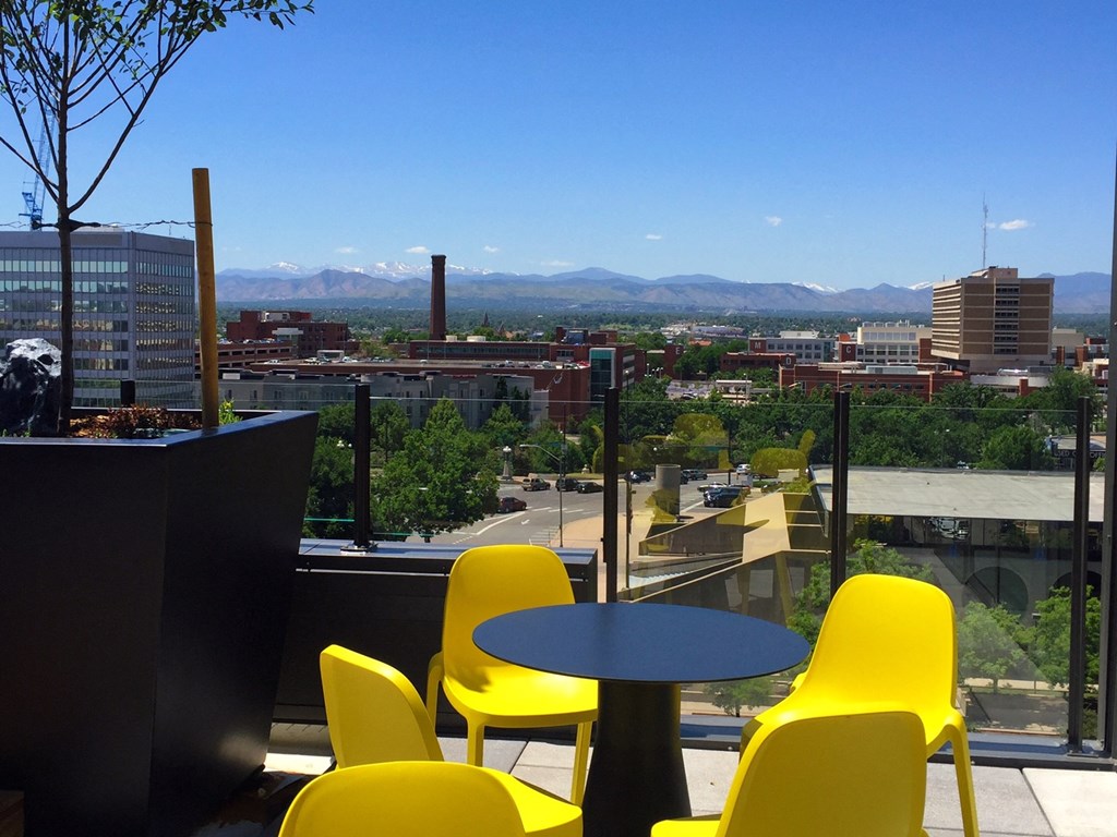 a balcony with yellow chairs and a table and a view of the city and mountains
