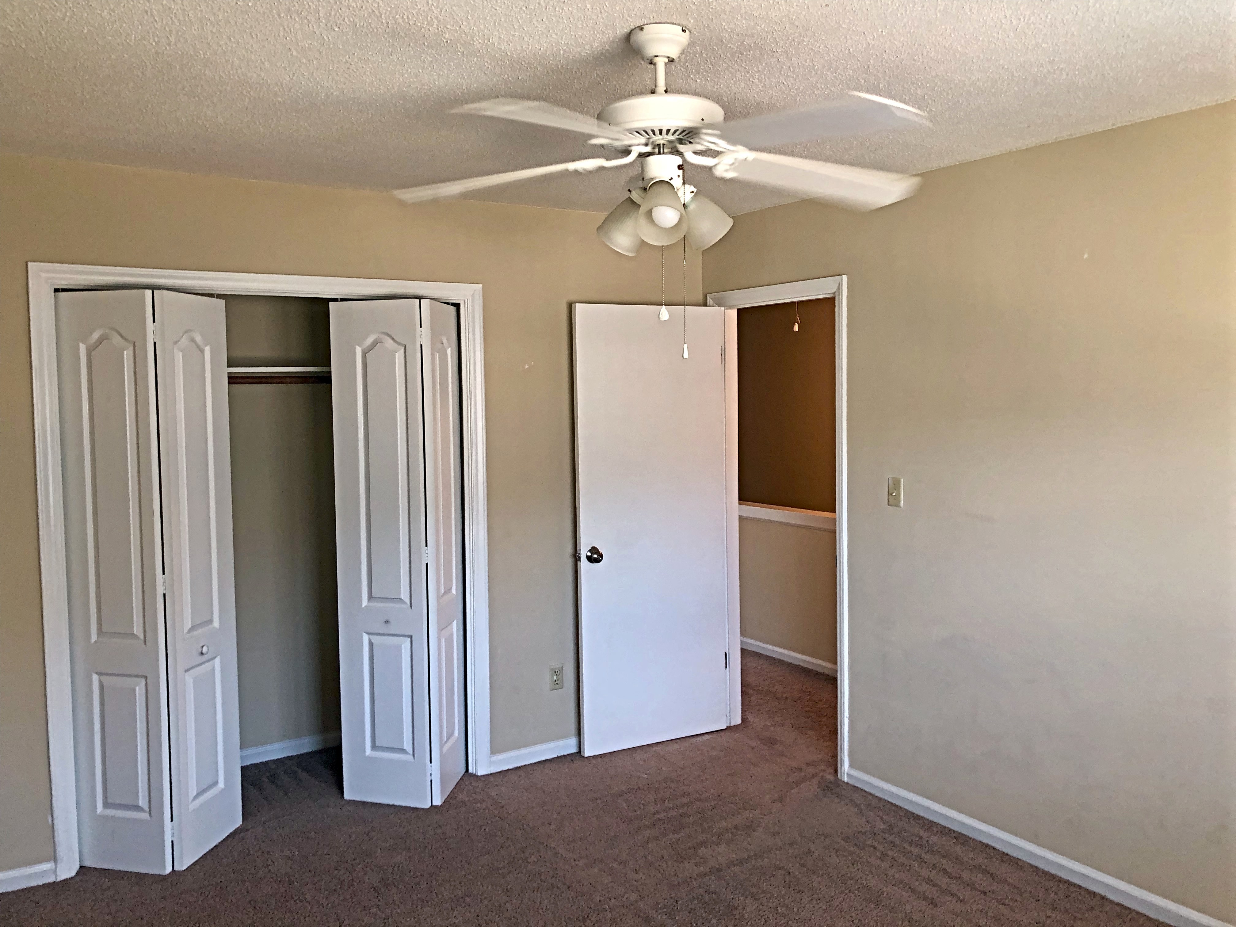 A room with a ceiling fan and three doors.